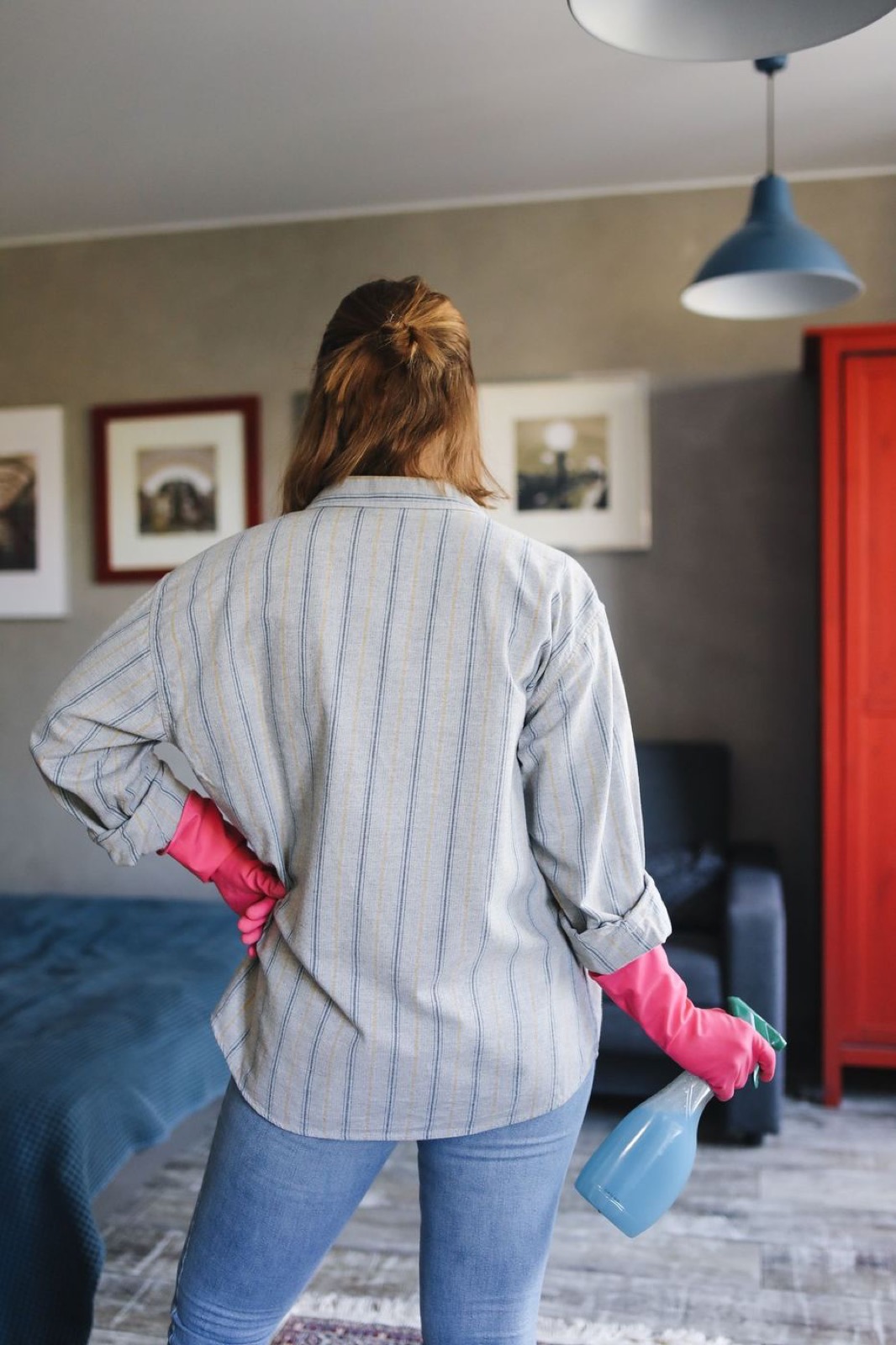 Housekeeper in pink gloves holding a spray bottle in a tidy bedroom