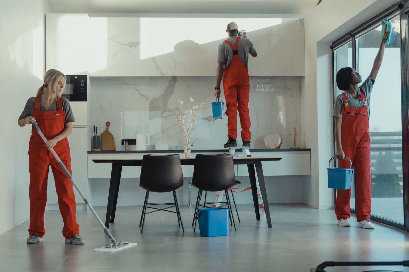 Cleaning team mopping, dusting, and washing windows in an open dining area