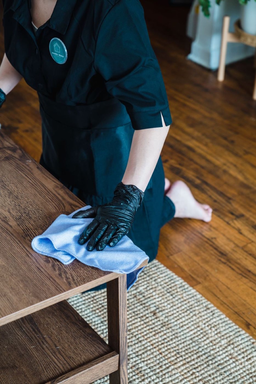 Housekeeper in black gloves wiping down a wooden coffee table during a regular house cleaning