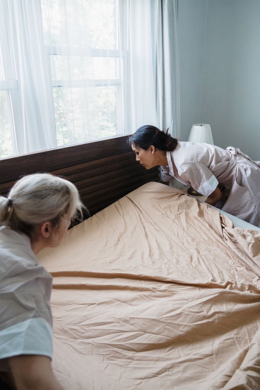 Two housekeepers changing the sheets on a guest bed during a vacation rental turnover